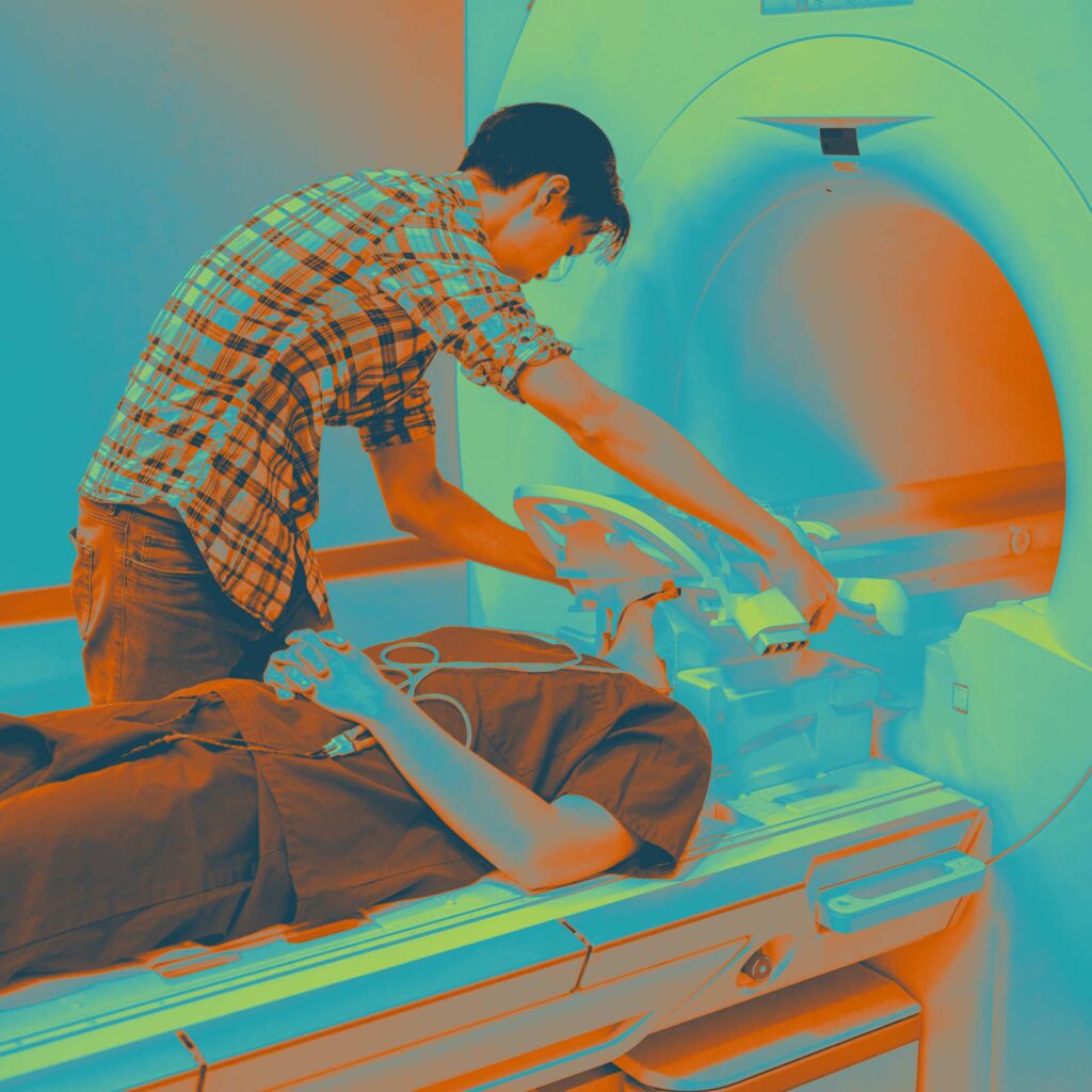 Student working with another student connected to health diagnostics machine and entering an MRI machine